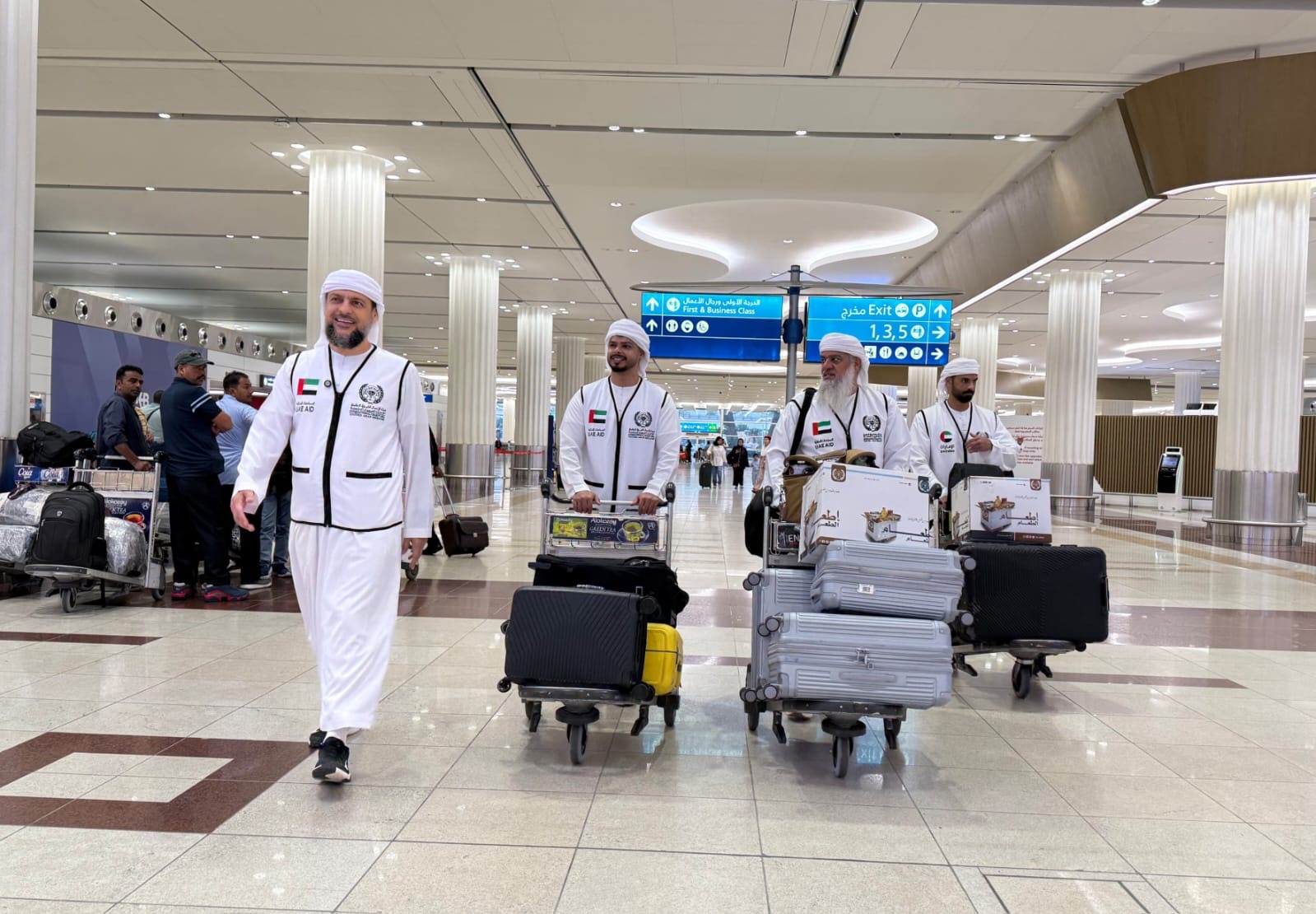 A delegation from a UAE charity organization walks through an airport terminal carrying luggage and aid supplies while departing for a humanitarian mission during the Dhul Hijjah season.